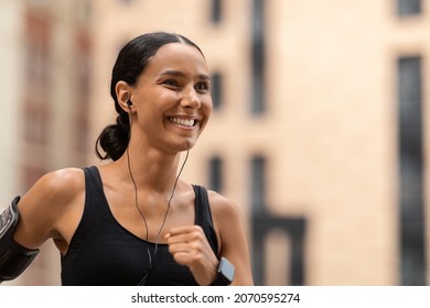 Fitness Lifestyle. Closeup Portrait Of Young Sporty Woman Jogging On Urban Street, Motivated Millennial Female Wearing Earphones Running Outdoors And Listening Her Favorite Music, Copy Space