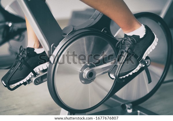 Fitness machine at home woman biking on indoor\
cycling stationary bike exercise indoors for cardio workout.\
Closeup of shoes on\
bicycle.