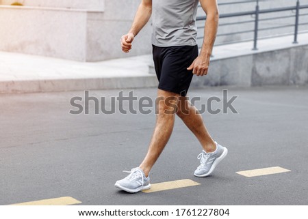 Fitness man athlete runner walking on the road. Person running working out living an active lifestyle training cardio in summer in sportswear and shoes. Lower body banner crop. Close up.
