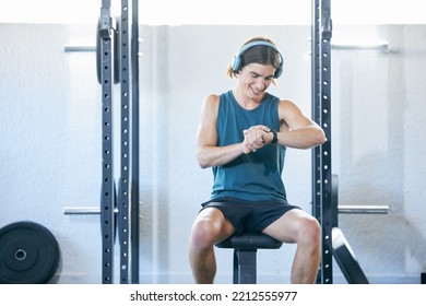 Fitness, Man Checking Time And Exercise For Sports Training Monitoring Workout While Sitting On A Bench At The Gym. Athletic Sport Male Looking At Watch While Resting On Equipment Indoors