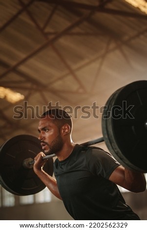 Fitness man doing back squats workout with heavy weight barbell. Sportsman doing exercise with heavy weights at old warehouse.