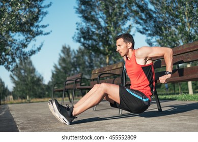 Fitness man doing bench triceps dips during outdoor cross training workout. Fit fitness sport model training outside using street furniture at an urban park.