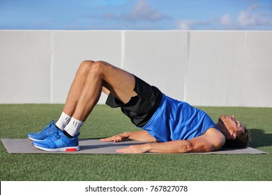 Fitness man doing bodyweight glute floor bridge pose yoga exercise. Fit athlete exercising glutes muscles with butt raise at summer outdoor gym instruction class on grass. - Powered by Shutterstock