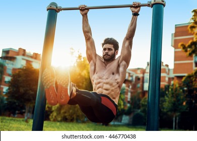 Fitness man doing stomach workouts on horizontal bar outdoors