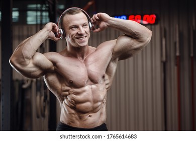 Fitness man with headphones at workout in gym. Bodybuilding healthy concept background - muscular fitness men doing exercises in gym naked torso. Good looking strong athletic rough man workout
