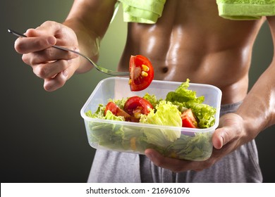 Fitness man holding a bowl of fresh salad on black background
