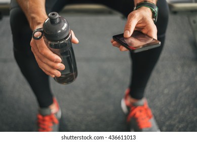 Fitness Man Looking To The Phone For Motivation Before Gym Workout. Sporty Male Athlete Looking His Smartphone Holding Water Bottle.