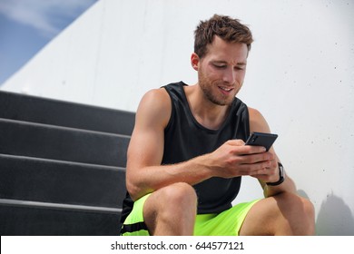 Fitness Man Runner Using Smart Phone Texting Sms Wearing Smartwatch For Cardio Activity Tracking. Active Male Jogger Sitting On Stairs.