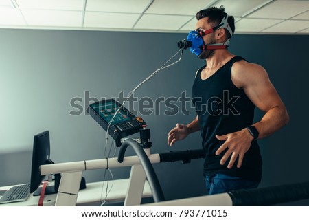 Fitness man running on treadmill with a mask testing his performance. Athlete examining his performance in sports science lab.