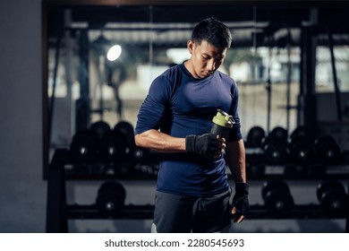 Fitness man in sportswear holding a bottle water or protein shake for drink in fitness gym. Health care and workout. Asian man replenishing water balance after workout. Concept of health and wellness. - Powered by Shutterstock