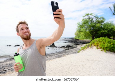 Fitness man taking selfie of himself after workout. Good looking young adult taking a self-portrait picture with his smartphone camera after exercising on a beach during summer vacation travel. - Powered by Shutterstock