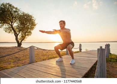 Fitness man training air squat exercise on beach outside. Fit male exercising crossfit outside. Young handsome caucasian male fitness model and instructor outdoors