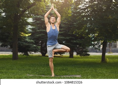 Fitness, man training yoga in tree pose outdoors. Young sporty guy makes breathing exercise in park, copy space