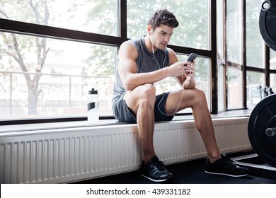 Fitness Man Wearing Sportswear Listening To Music Sitting On Windowcill