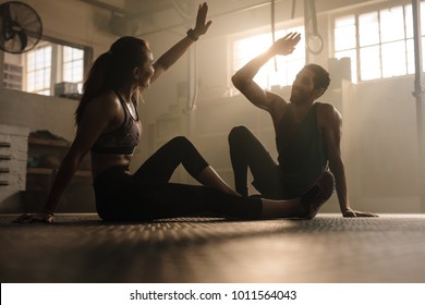 Fitness man and woman giving each other a high five after the training session in gym. Fit couple high five after workout in health club.