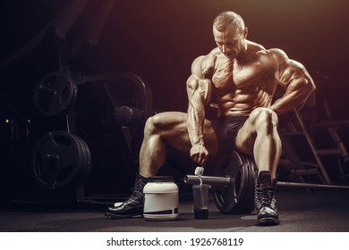 Fitness Man At Workout In Gym With Protein Powder Jar. Bodybuilding And Healthy Lifestyle Concept Background. Muscular Bodybuilder With Sport Nutrition Supplements Jar In Gym Naked Torso