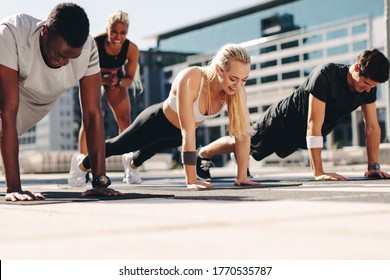 Fitness men and women doing push-ups with motivation from their female trainer outdoors in the city. - Powered by Shutterstock