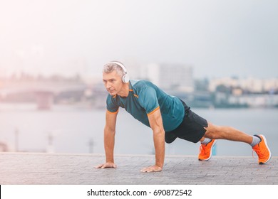 Fitness Middle Aged Man Doing Push-ups On The Riverside. Male Athlete Exercising Outdoors. Sports And Active Lifestyle.