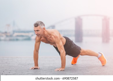 Fitness middle aged man doing push-ups on the riverside. Male athlete exercising outdoors. Sports and active lifestyle.