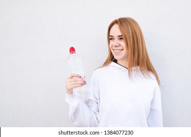 Fitness Model Holding A Water Bottle In In Hand, Looking Sideways And Smiling. Happy Sporty Girl With A Bottle Of Water In Hands, Smiling, Isolated On White Background. Healthy Drink And Sport Concept