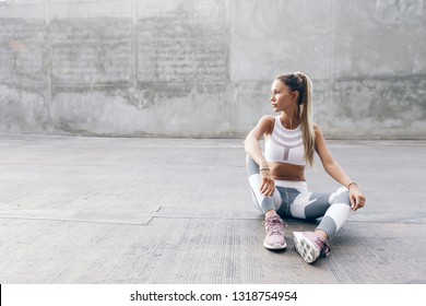 Fitness model in sportswear posing on the city street over gray concrete background. Outdoor sports clothing and shoes, urban style.