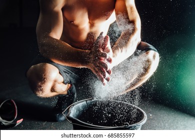 Fitness model trainer rubs his hands with chalk and talc so that fingers do not slip or slide. Black bucket, lens flare. Strong Clap with Cloud of dust. - Powered by Shutterstock