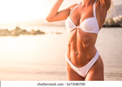 Fitness muscles abdominal belly female body - concept of diet and workout for young people - white bikini and sunbath in holiday summer vacation - sea in background - unrecognizable girl - Powered by Shutterstock