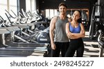 Fitness muscular couple posing in gym, strong couple standing in sports center surrounded by exercise equipment and smiling at camera