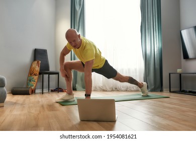 Fitness Online. Concentrated Mature Male Personal Trainer In Sportswear Conducting Online Training At Home, Exercising While Having Virtual Fitness Class On Laptop. Sport And Healthy Lifestyle Concept