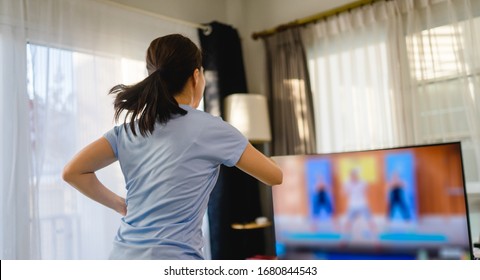 健身在線留在家。家健身課直播在線直播。亞洲女性進行力量訓練有氧運動。在家的客廳裏觀看智能電視視頻。