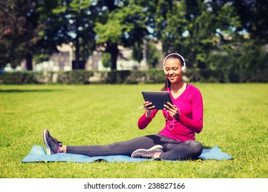 Fitness, Park, Technology And Sport Concept - Smiling African American Woman With Tablet Pc Computer And Headphones On Mat Outdoors