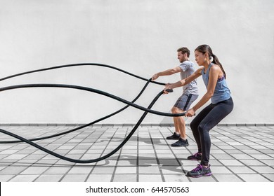 Fitness people exercising with battle ropes at gym. Woman and man couple training together doing battling rope workout working out arms and cardio for cross fit exercises.