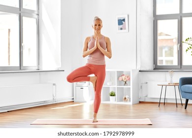 fitness, people and healthy lifestyle concept - happy smiling young woman doing yoga in tree pose at home