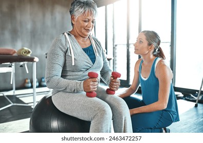 Fitness, personal trainer and senior woman with dumbbell in gym for physiotherapy, support or workout. Lens flare, coach and elderly patient on ball for help, arthritis training or rehabilitation - Powered by Shutterstock