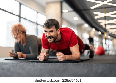 Fitness and plank with personal trainer during workout core exercise training at gym for strong abdominal muscles. Sporty guy coaching young woman gym client on individual yoga mat practicing plank. - Powered by Shutterstock