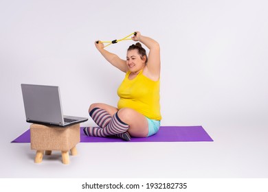 Fitness Plus Size Woman, Online Personal Trainer, Home Training, Technology, Diet. Overweight Woman Doing Stretching Exercises With Resistance Band Sitting On A Fitness Mat At Home, Using Laptop.