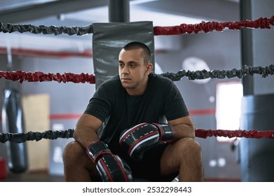 Fitness, rest and man in ring for boxing, relax or thinking in gym after training for competition. Professional boxer, tired athlete or break for sport, workout or exercise with fatigue at fight club - Powered by Shutterstock