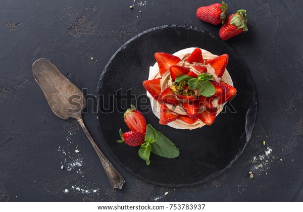 Fitness restaurant
dessert at black background. Anna Pavlova meringue with low-fat
whipped cream and fresh strawberry on slate and cake spatula aside,
top view, copy space