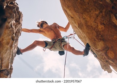 Fitness, Rock Climbing And Strong Mountain Climber On A Cliff With Ropes In Summer Challenge And Extreme Exercise. Danger, Courage And Healthy Man Fearless, Sports And Big Rocks Or Stone Below View