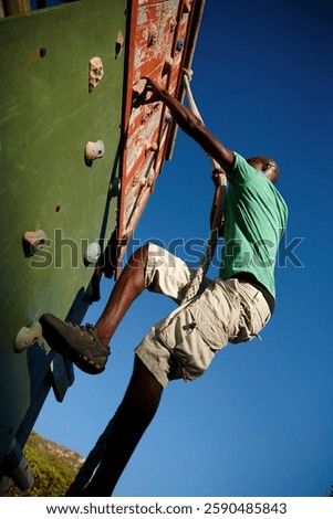 Fitness, rope and black man climbing wall for training, endurance exercise and bootcamp challenge. Military barrier, below and physical test for outdoor workout, obstacles and strength assessment