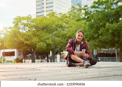 Fitness Runner On Mobile Smart Phone App Tracking Progress. Athlete Mature Woman In Sportswear Listening Music With Earphones On City Street. Woman Sitting On Floor And Using Smartphone, Copy Space.