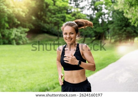Fitness runner smiling at camera while jogging in city park