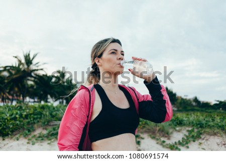 Fitness runner woman drinking water of a sport bottle. Athlete girl taking a break during run to hydrate during hot summer exercise on beach. Healthy active lifestyle.