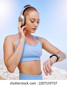 Fitness, runner and woman on time by her smartwatch as she monitors her performance, heartbeat and pulse outdoors. Headphones, health and girl running in summer streaming music, radio song or podcast - Shutterstock ID 2207159737
