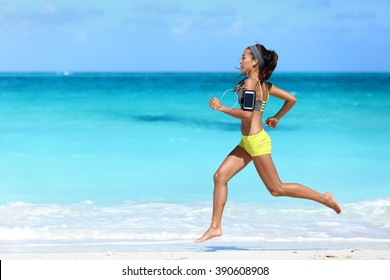 Fitness Runner Woman Running On Beach Listening To Music Motivation With Phone Case Sport Armband Strap. Sporty Athlete Training Cardio Barefoot With Determination Under Summer Sun.