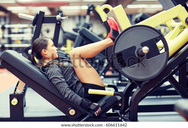 fitness,\
sport, bodybuilding, exercising and people concept - young woman\
flexing muscles on leg press machine in\
gym