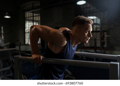 fitness, sport, bodybuilding and people concept - young man doing triceps dip exercise on parallel bars in gym