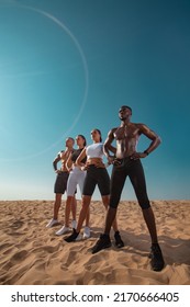 Fitness And Sport Concept. Group Of Four Young Sportsmens Women And Men, Fit Athletes Are Standing On The Sky Background Before Run. Healthy Lifestyle. Friends In Black And White Sportswear.