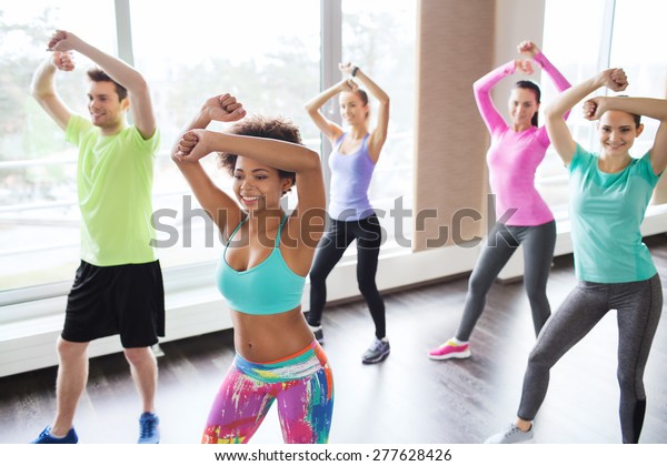fitness, sport,
dance and lifestyle concept - group of smiling people with coach
dancing zumba in gym or
studio