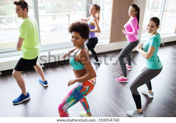 fitness, sport,\
dance and lifestyle concept - group of smiling people with coach\
dancing zumba in gym or\
studio